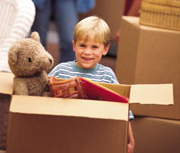 Smiling young boy standing in the midst of boxes full of items, including one with a teddy bear inside it